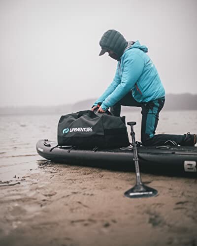 Person in blue jacket on paddleboard organizing gear